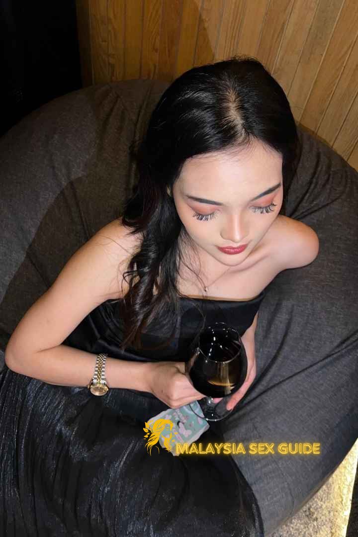 Woman in black dress holding a wine glass. KL Escort Outcall services.