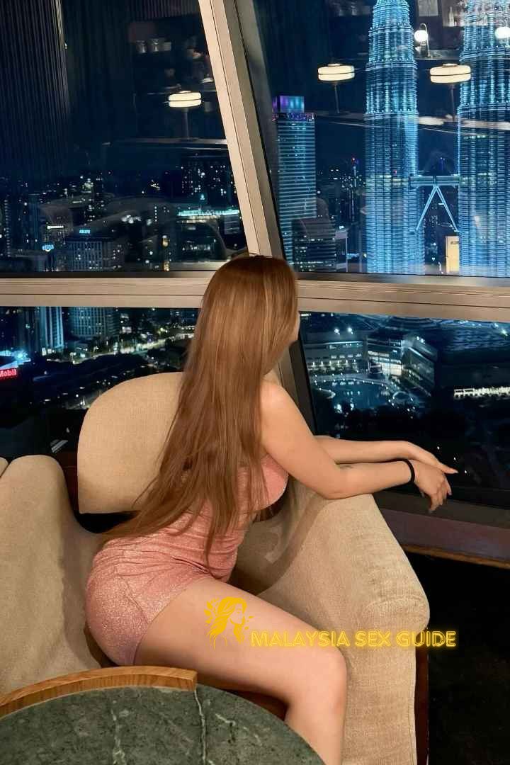 Woman enjoying city view from KL high-rise, wearing pink dress.