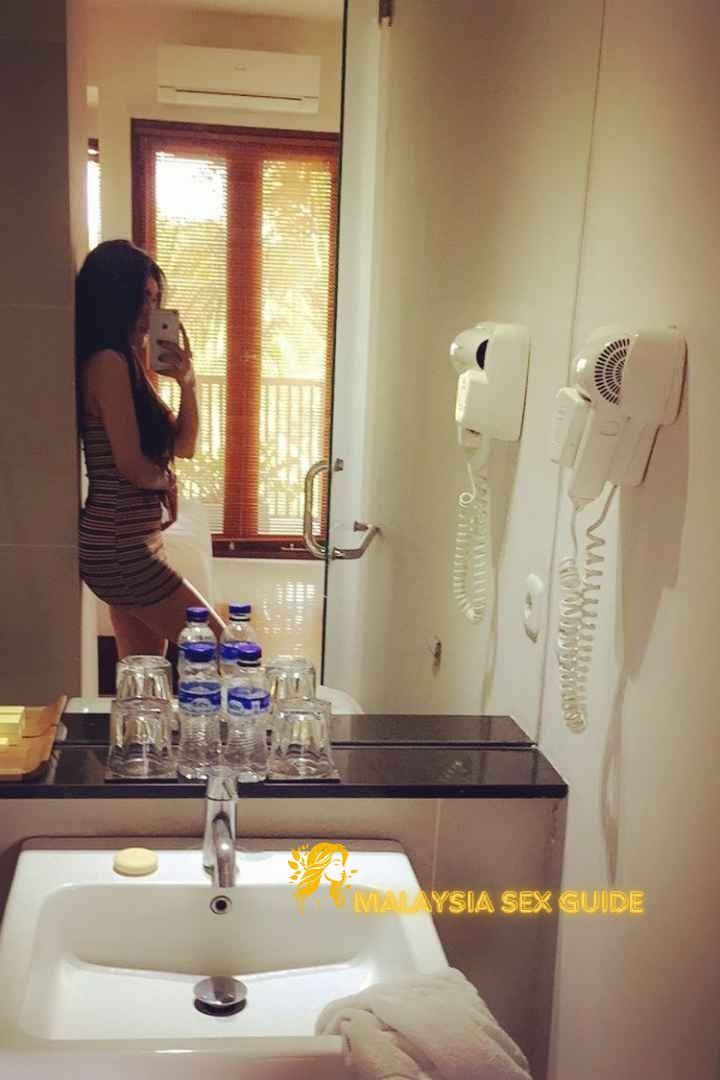 Woman in striped dress reflected in bathroom mirror. KL Escort.