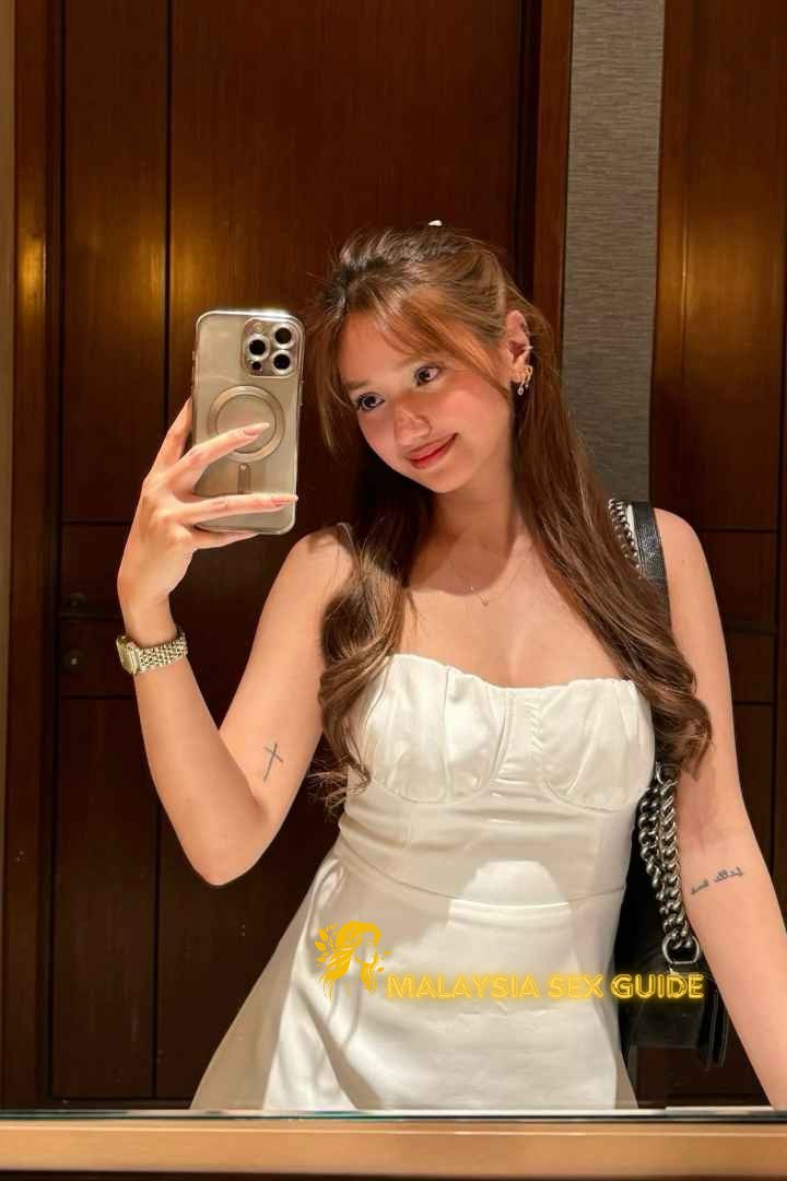 Attractive young woman in white dress taking a selfie. KL Escort Outcall.