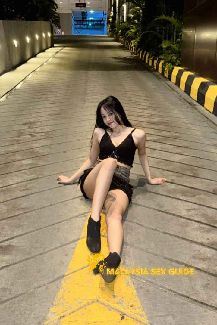 Young woman in black top and short skirt sitting on a road in Kuala Lumpur.