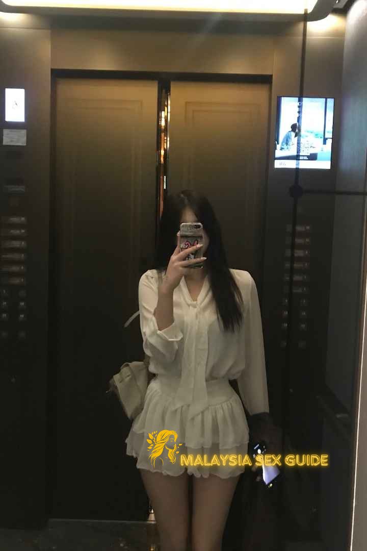 Young woman in white dress taking a selfie in an elevator.